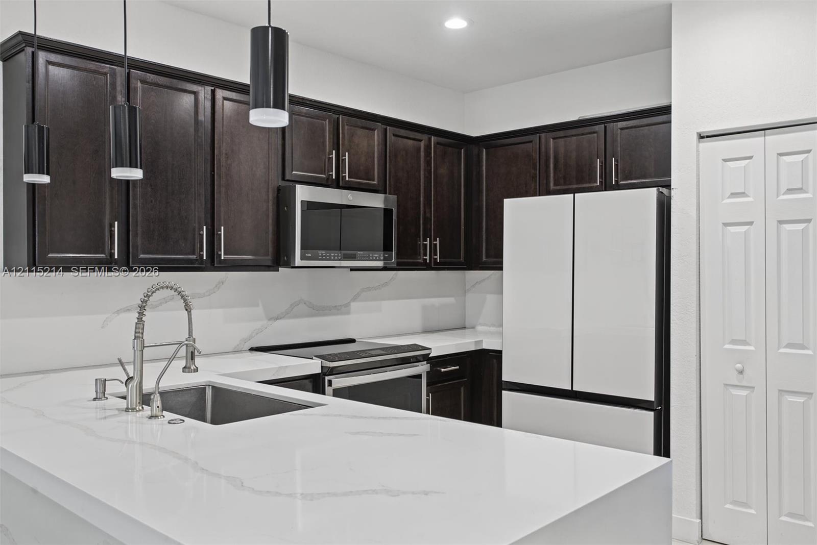 Kitchen featuring dark-toned cabinetry, white stone countertops with integrated backsplash, stainless steel appliances, stainless steel faucet with pu