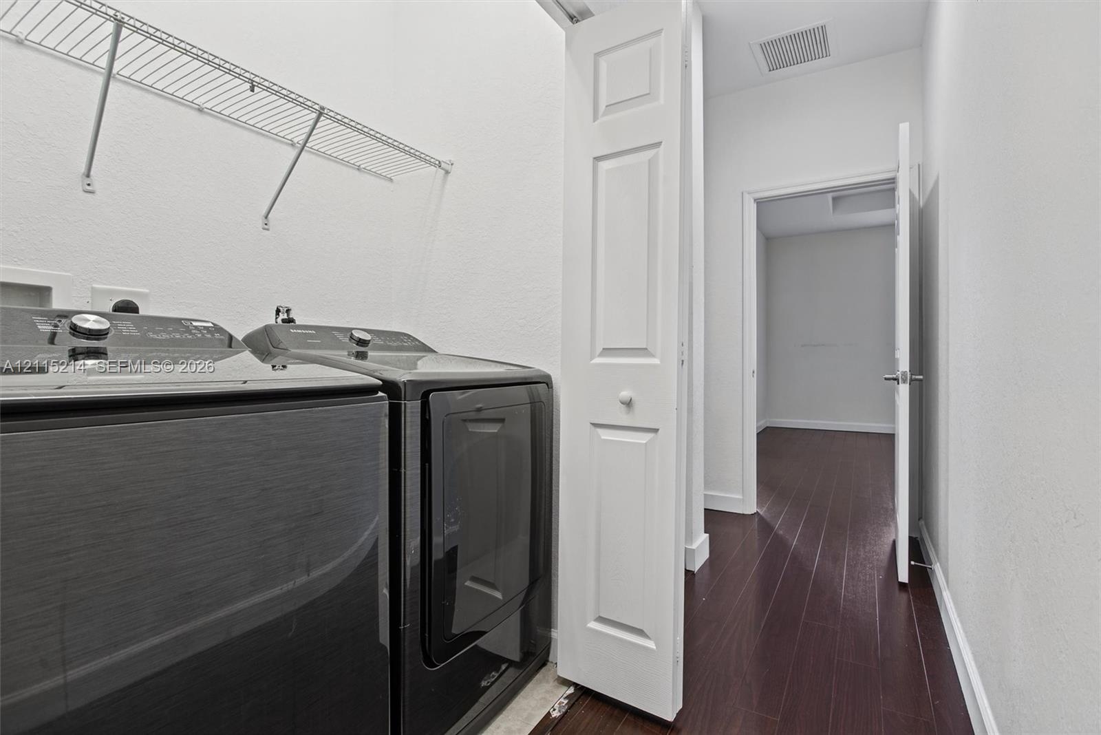 Dedicated laundry area featuring dark-toned washer and dryer, white bi-fold closet doors, wire shelving, and wood-finish flooring