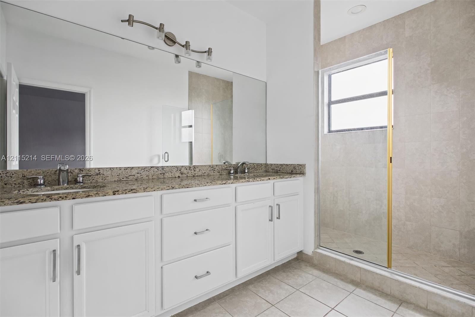 Double vanity featuring white cabinetry, stone-surface countertop, dual drop-in sinks, full-width mirror, and a walk-in shower with tiled surround and