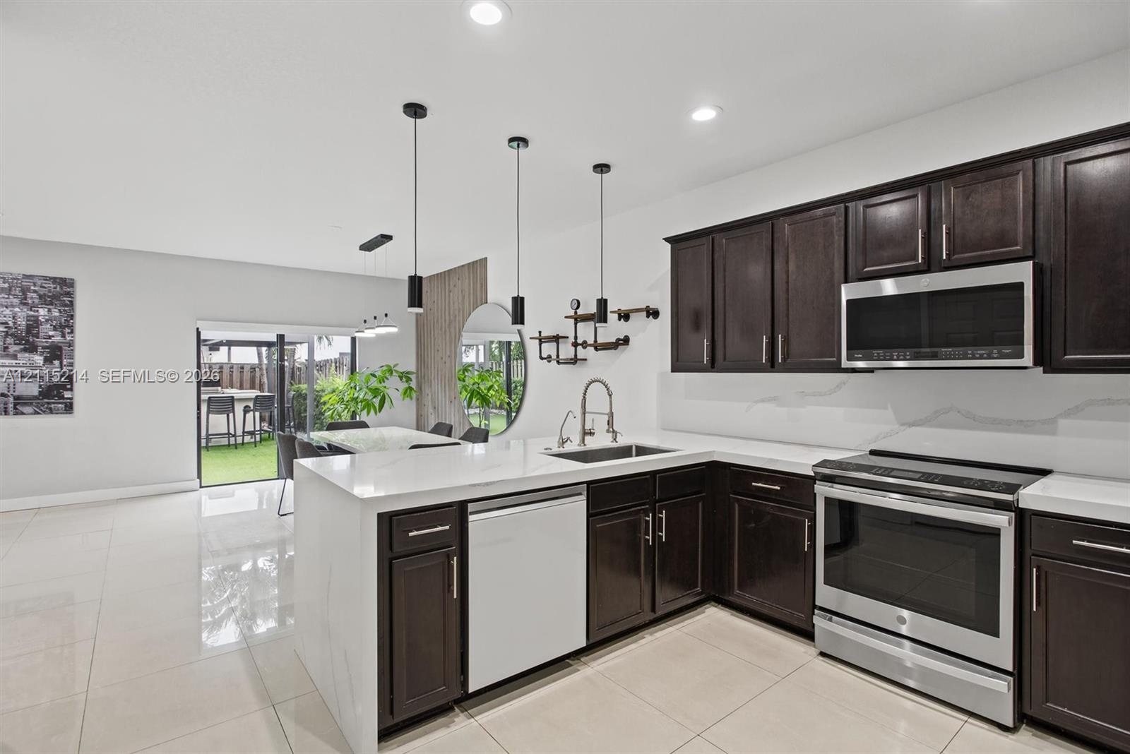 Kitchen featuring dark-finish cabinetry, white solid-surface countertops, stainless steel appliances, recessed ceiling lighting, and large-format tile