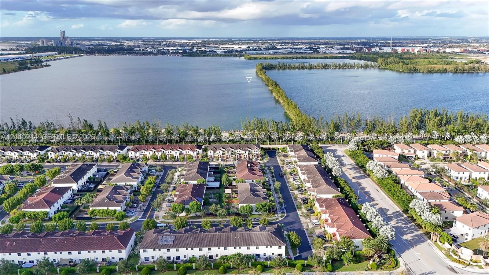 Aerial perspective of multi-family residences featuring tile roofing, paved streets, manicured green space, and proximity to large bodies of water