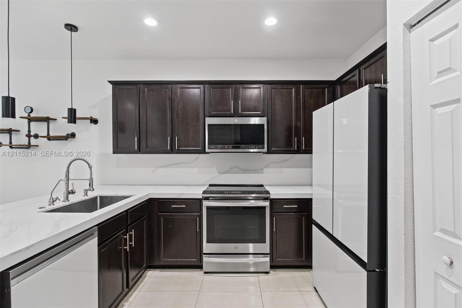 Kitchen featuring dark-finish cabinetry, stone-style countertops, stainless steel appliances, a recessed sink with a high-arch pull-down faucet, and i
