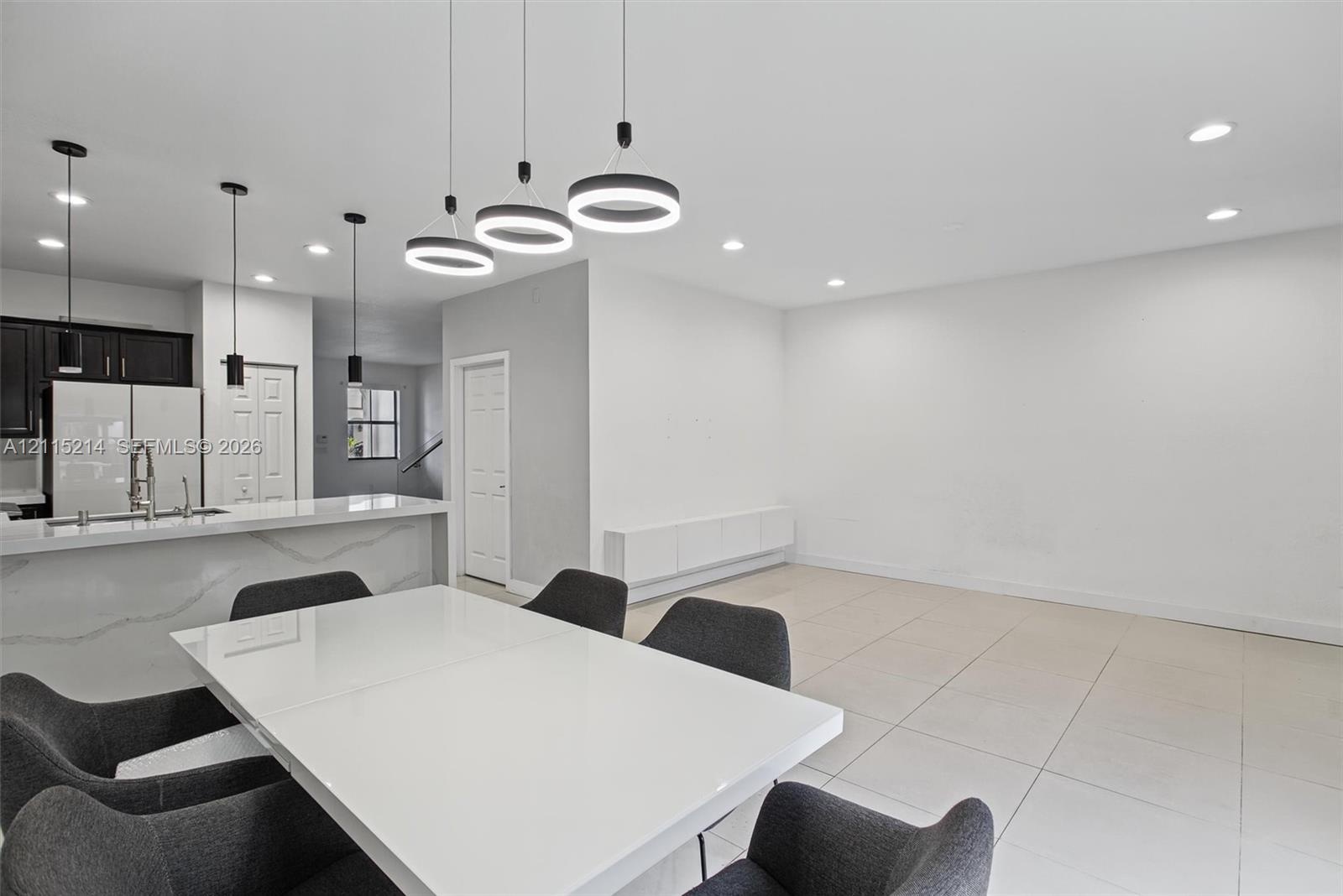 Modern open-concept area featuring large-format tile flooring, a kitchen peninsula with a stone-surfaced waterfall edge, custom pendant lighting, and 