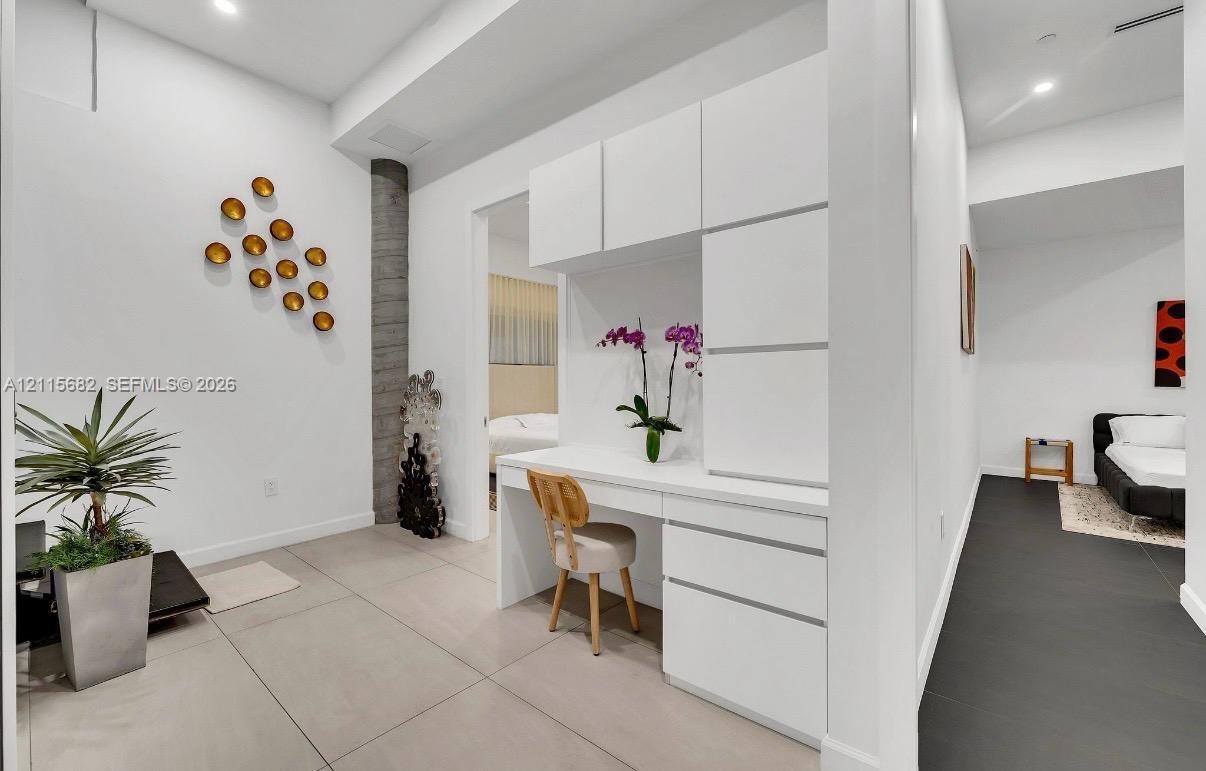 Built-in white cabinetry with integrated desk surface, large-format tile flooring, and vertical stone-texture architectural column
