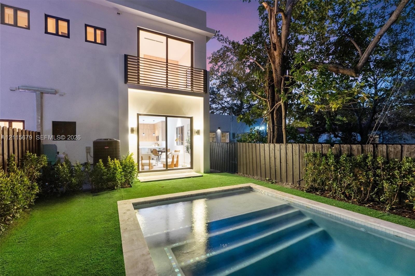 Modern exterior featuring a swimming pool with integrated stairs, synthetic lawn, wood-slat upper balcony railing, and floor-to-ceiling sliding glass 