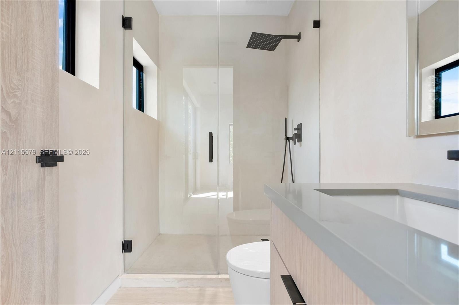 Bathroom featuring a wood-finish vanity with a stone countertop, a glass-enclosed walk-in shower with matte black rainfall showerhead, and high-contra