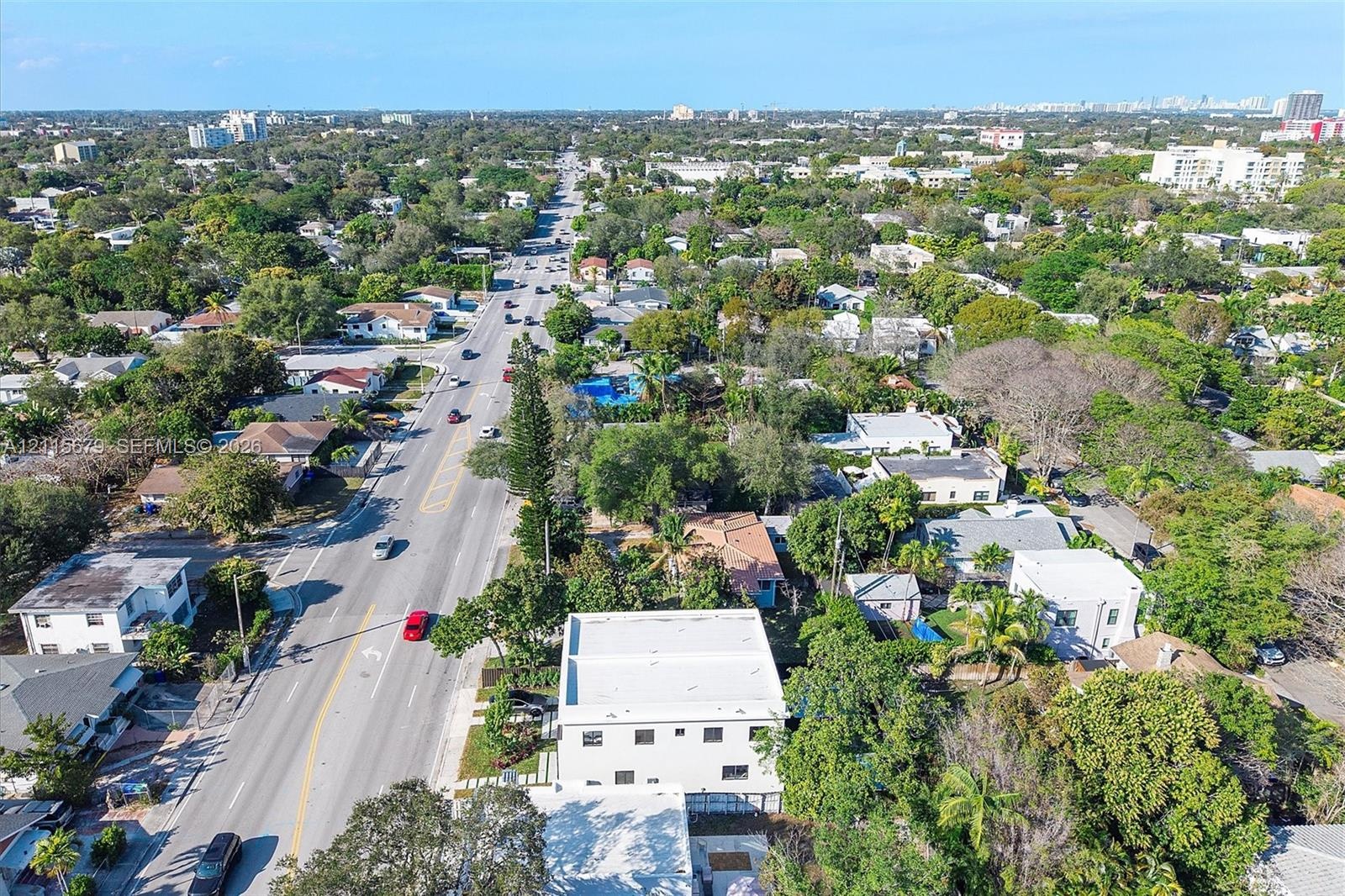Aerial perspective of a multi-story structure featuring a flat roof and concrete-finish exterior, situated on a lot with established canopy trees and 