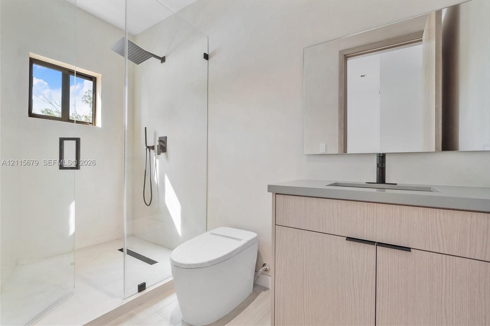 Modern bathroom featuring a wood-finish vanity, solid-surface countertop, frameless glass-enclosed shower, wall-mounted matte black fixtures, and a sl