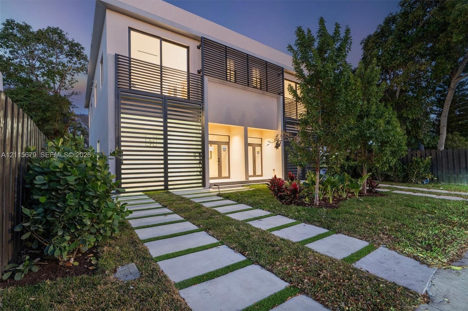 Contemporary two-story exterior featuring a smooth stucco finish, horizontal metal louvered privacy screening, glass sliding doors, and a linear paver