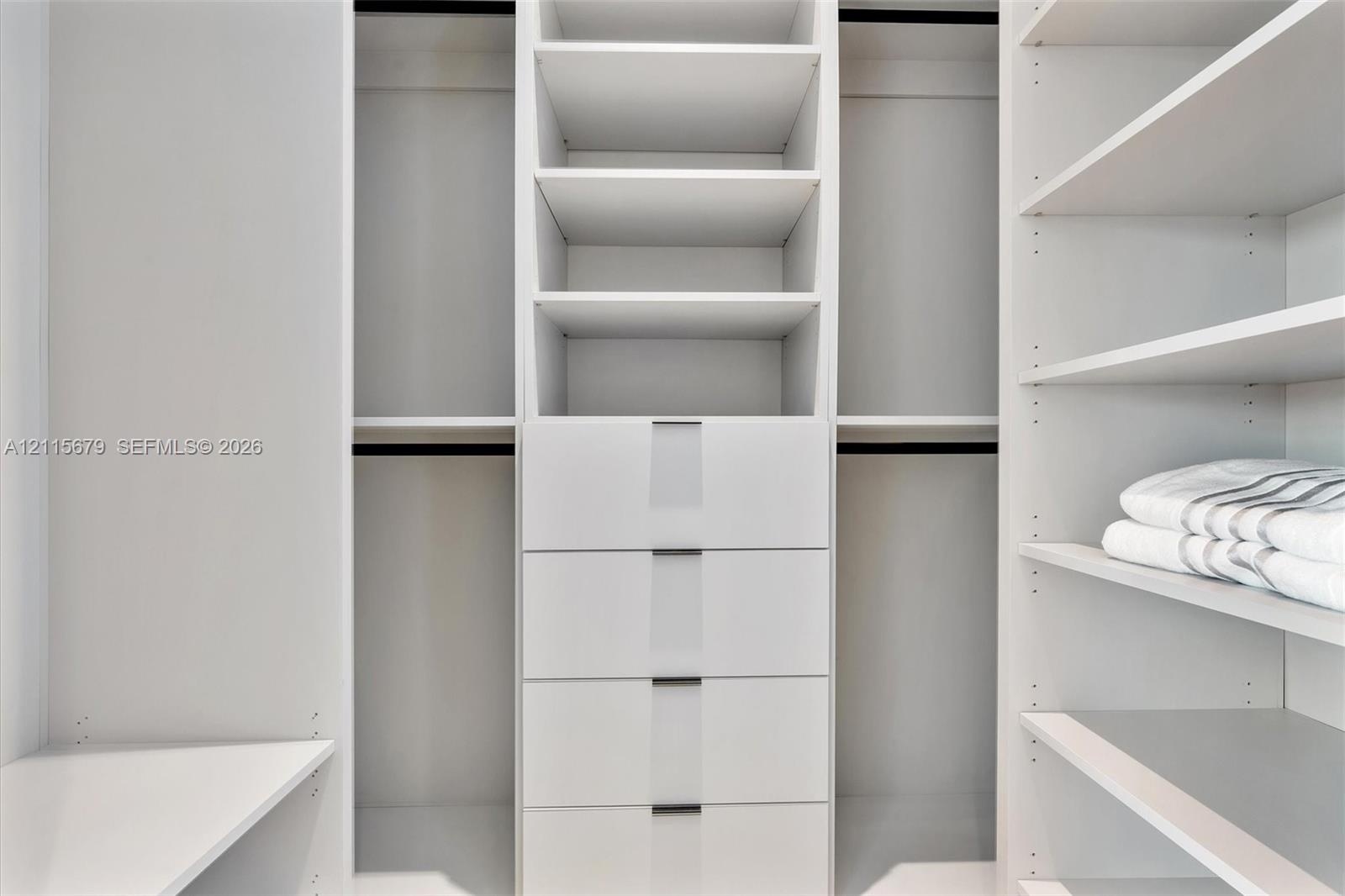 Custom walk-in closet featuring white built-in shelving, four integrated storage drawers, and multiple hanging sections
