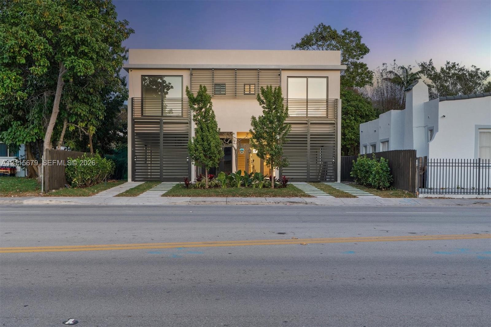 Contemporary two-story exterior featuring a smooth stucco finish, vertical metal louvers, expansive floor-to-ceiling glass panels, and dual concrete p