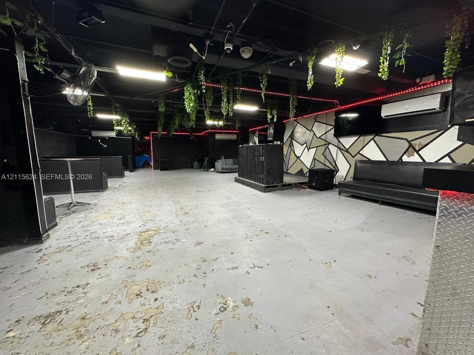 Open-concept space featuring industrial-style exposed black ceiling, geometric wall accents, wall-mounted ductless climate control units, and polished