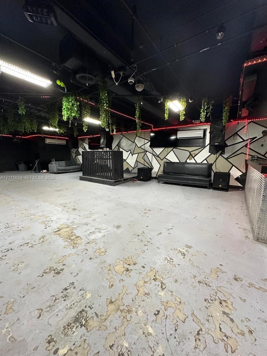 Open-concept floor plan with geometric wall mural, exposed ceiling with industrial lighting, raised platform stage, and metal-panel bar facade