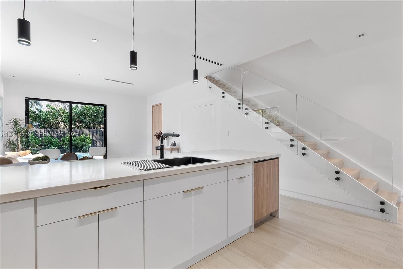 Modern kitchen island featuring a quartz countertop, black undermount sink, and matte black faucet, complemented by white cabinetry, wood-finish floor