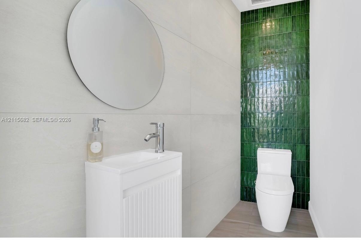 Wall-mounted circular mirror, white vanity with fluted cabinetry, polished chrome faucet, floor-to-ceiling green glazed tile accent wall, and porcelai