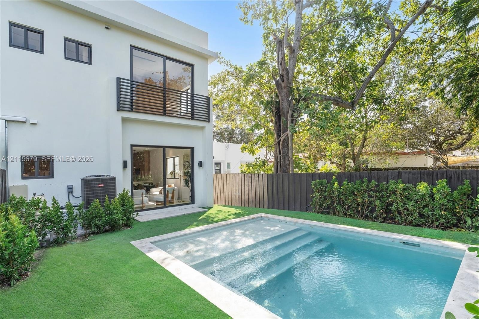 Two-story stucco exterior featuring a second-level balcony with horizontal metal railing, a swimming pool with integrated stairs, and a manicured lawn