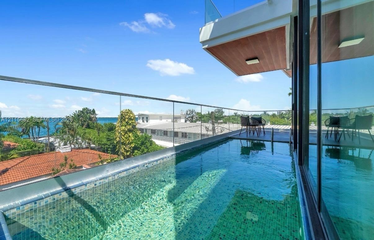Elevated plunge pool featuring mosaic tile surfacing and a seamless glass railing, complemented by an overhead wood-finished balcony soffit and large-