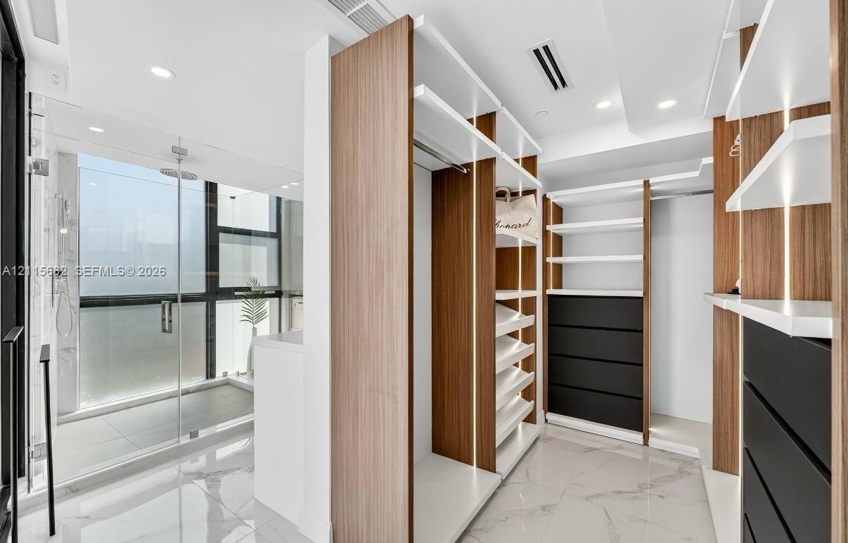 Custom walk-in closet featuring wood-finish cabinetry, built-in shelving, integrated LED accent lighting, and matte black drawer fronts