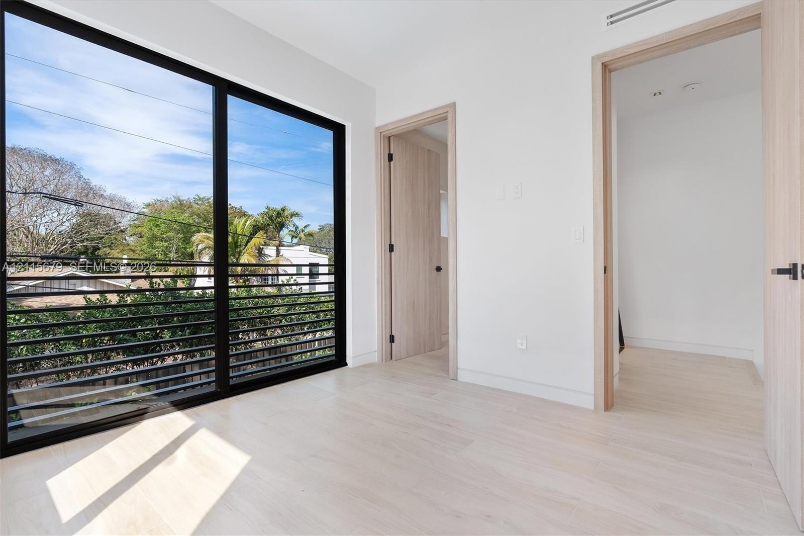 Floor-to-ceiling windows with black framing, wood-finish interior doors, light-toned wood-finish flooring, and black metal horizontal exterior railing