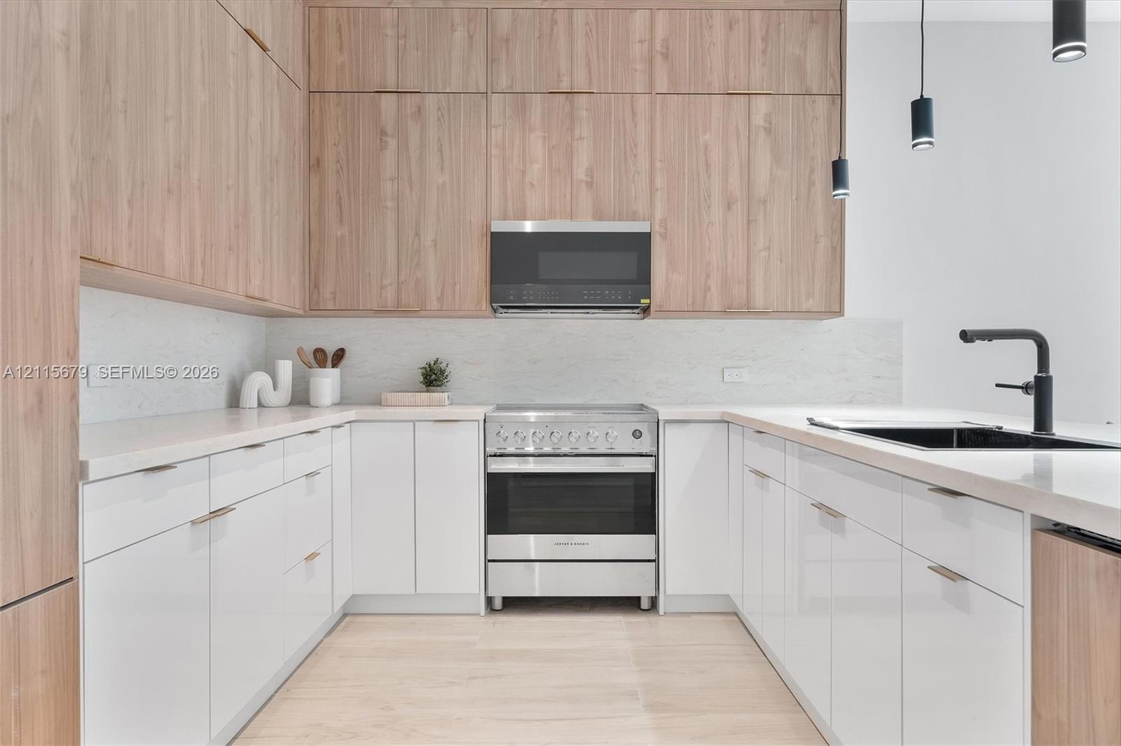 Kitchen featuring floor-to-ceiling wood-finish cabinetry, gloss white lower cabinetry, light-toned stone-finish countertops, stainless steel gas range