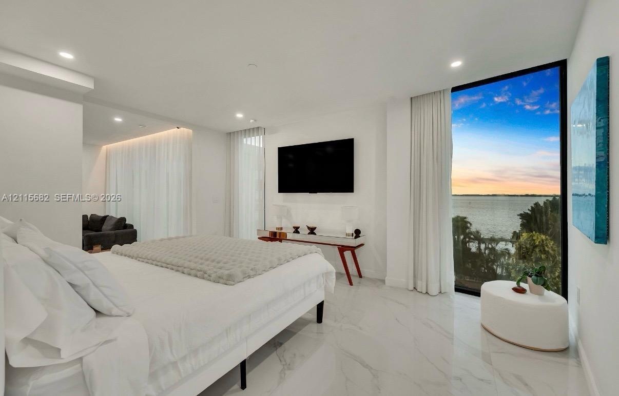 Floor-to-ceiling black-framed windows, large-format stone-finish flooring, recessed lighting, cove lighting, and water backdrop