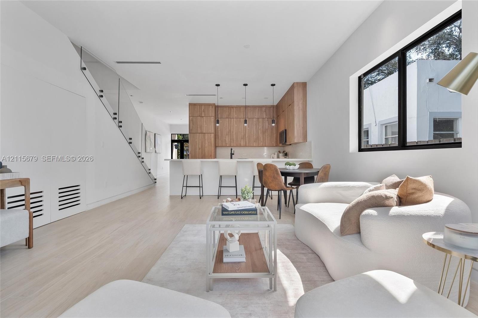 Open-concept interior featuring light wood-finish flooring, custom wood-veneer cabinetry, a center island with bar seating, and a glass-paneled stairc