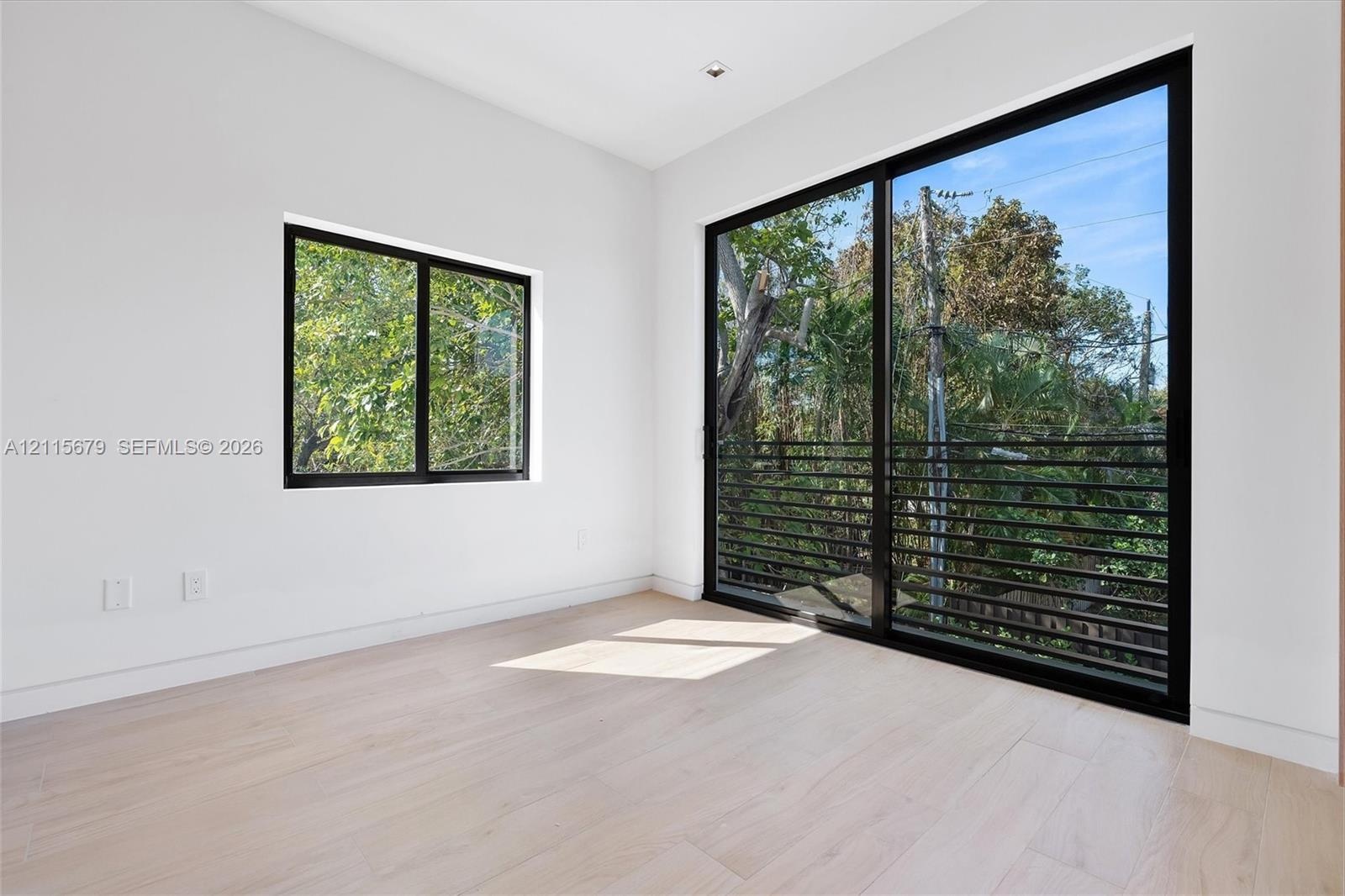 Neutral interior space featuring wood-finish flooring, floor-to-ceiling sliding glass doors, a secondary window, and matte black framing