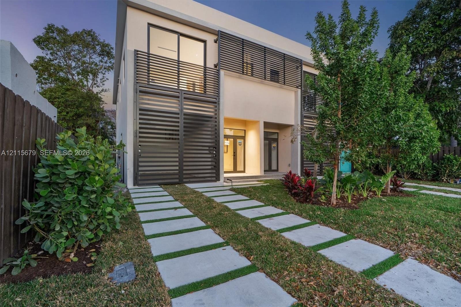 Modern two-story residence featuring a smooth stucco exterior, horizontal metal privacy screening, integrated balcony, and a permeable paver driveway 