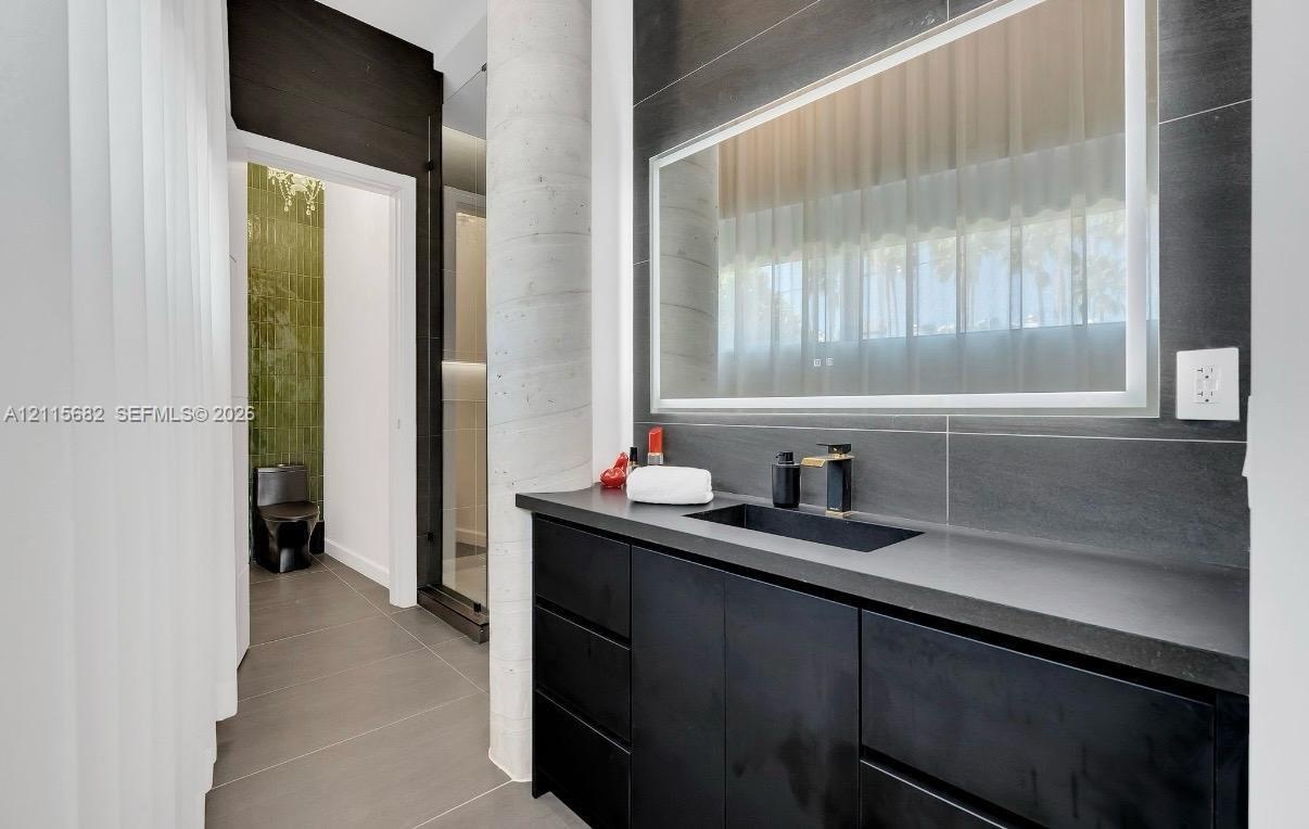 Modern vanity featuring dark cabinetry, a solid-surface countertop, an integrated rectangular sink, and a wall-mounted faucet, accented by a backlit m