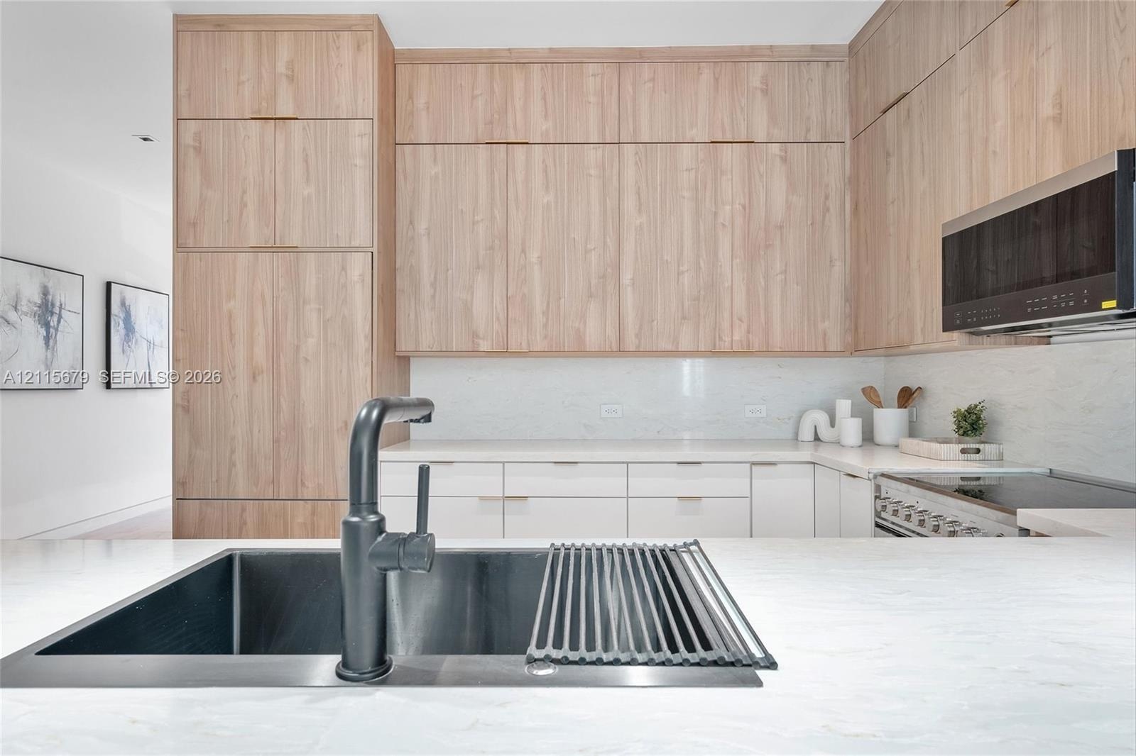 Kitchen featuring floor-to-ceiling wood-finish cabinetry, white stone-finish countertops, matte black single-handle faucet, integrated stainless steel