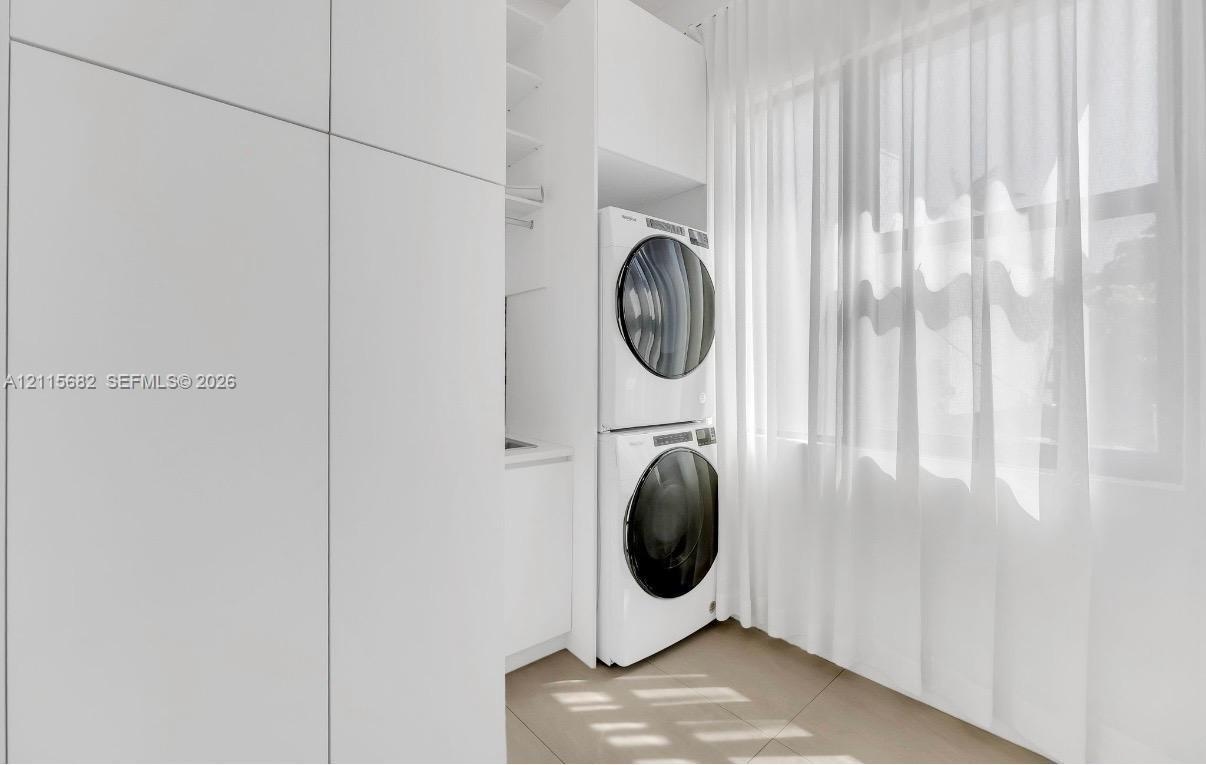 Laundry space featuring floor-to-ceiling white cabinetry, integrated stacking appliance housing, and tile flooring