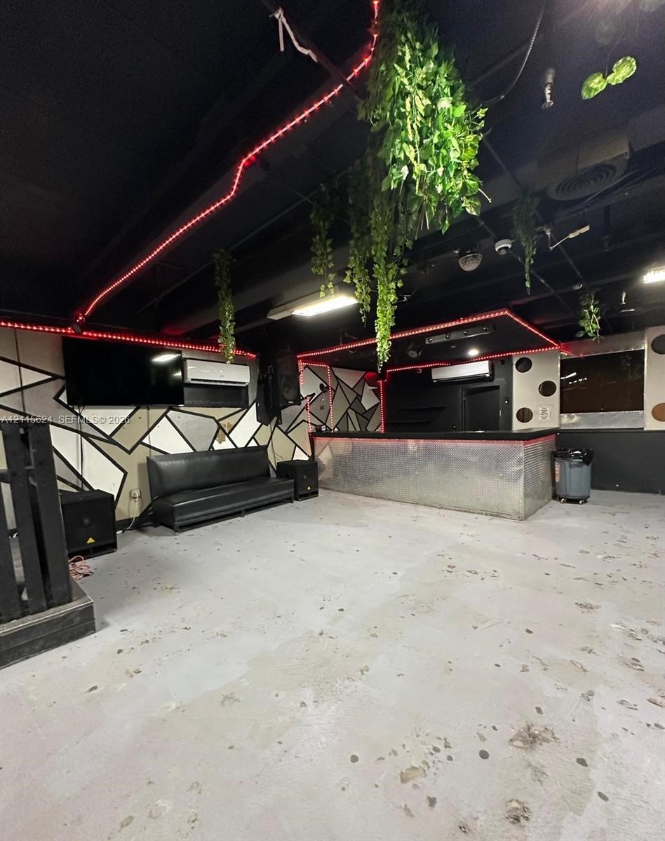Built-in bar with metallic frontage, geometric patterned accent walls, wall-mounted ductless climate control units, and industrial-style exposed ceili
