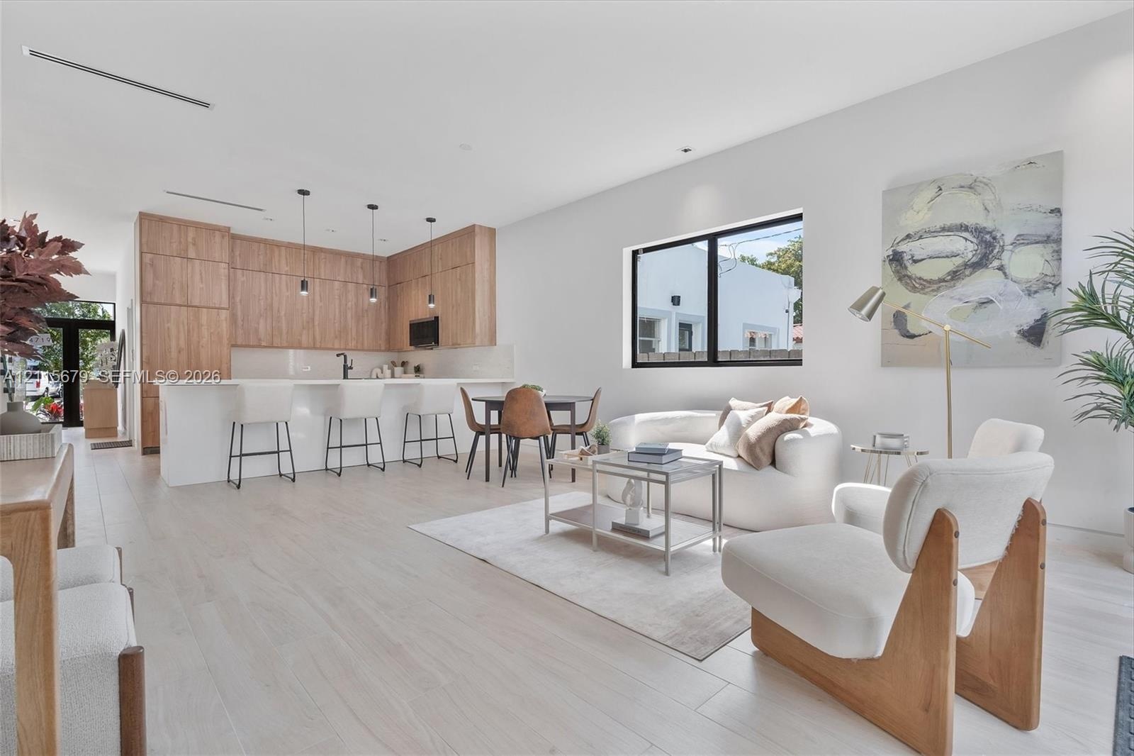 Open-concept living space featuring wood-finish cabinetry, a large kitchen island with quartz-surface countertops, light-toned wood-finish flooring, a