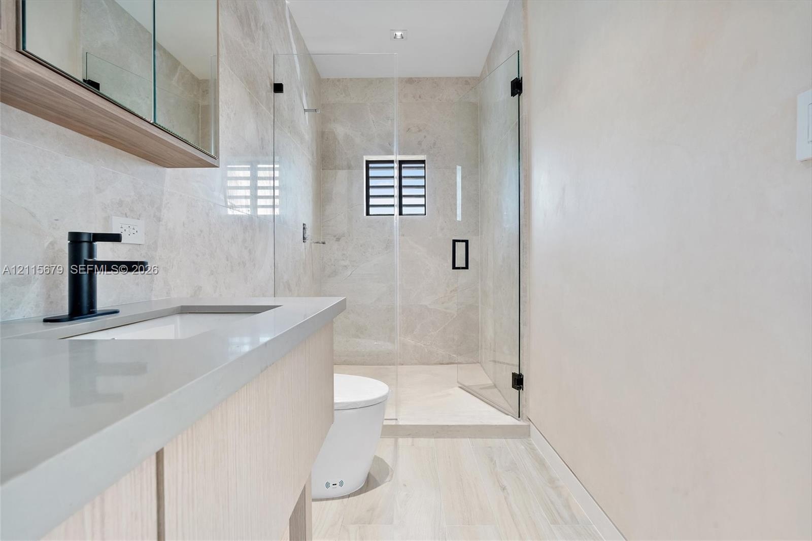 Bathroom featuring a wood-finish floating vanity, matte black faucet, full-height tile shower enclosure with a glass door, and large-format tile floor