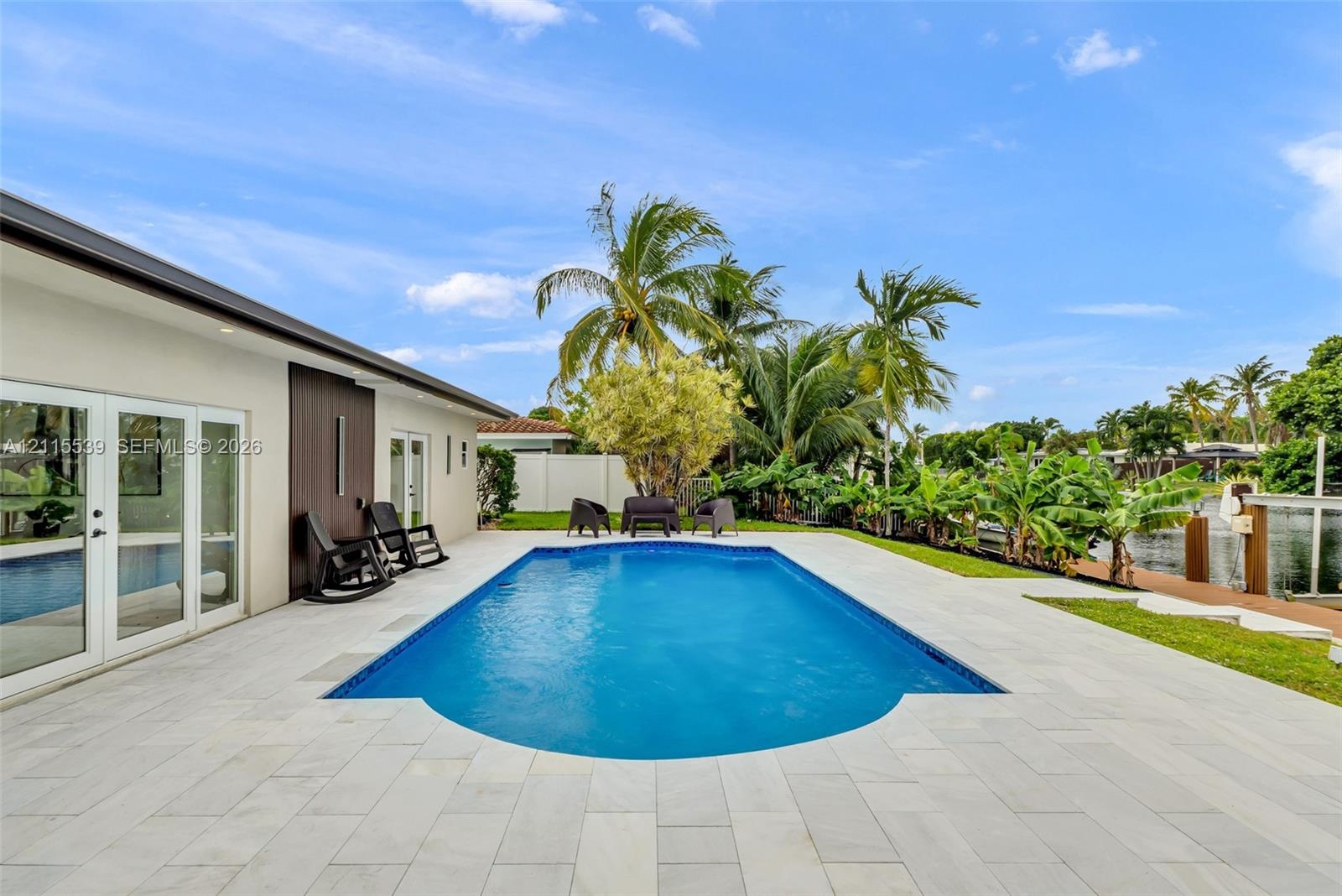 In-ground swimming pool with stone-tile decking, waterfront bulkhead, and mature tropical landscaping