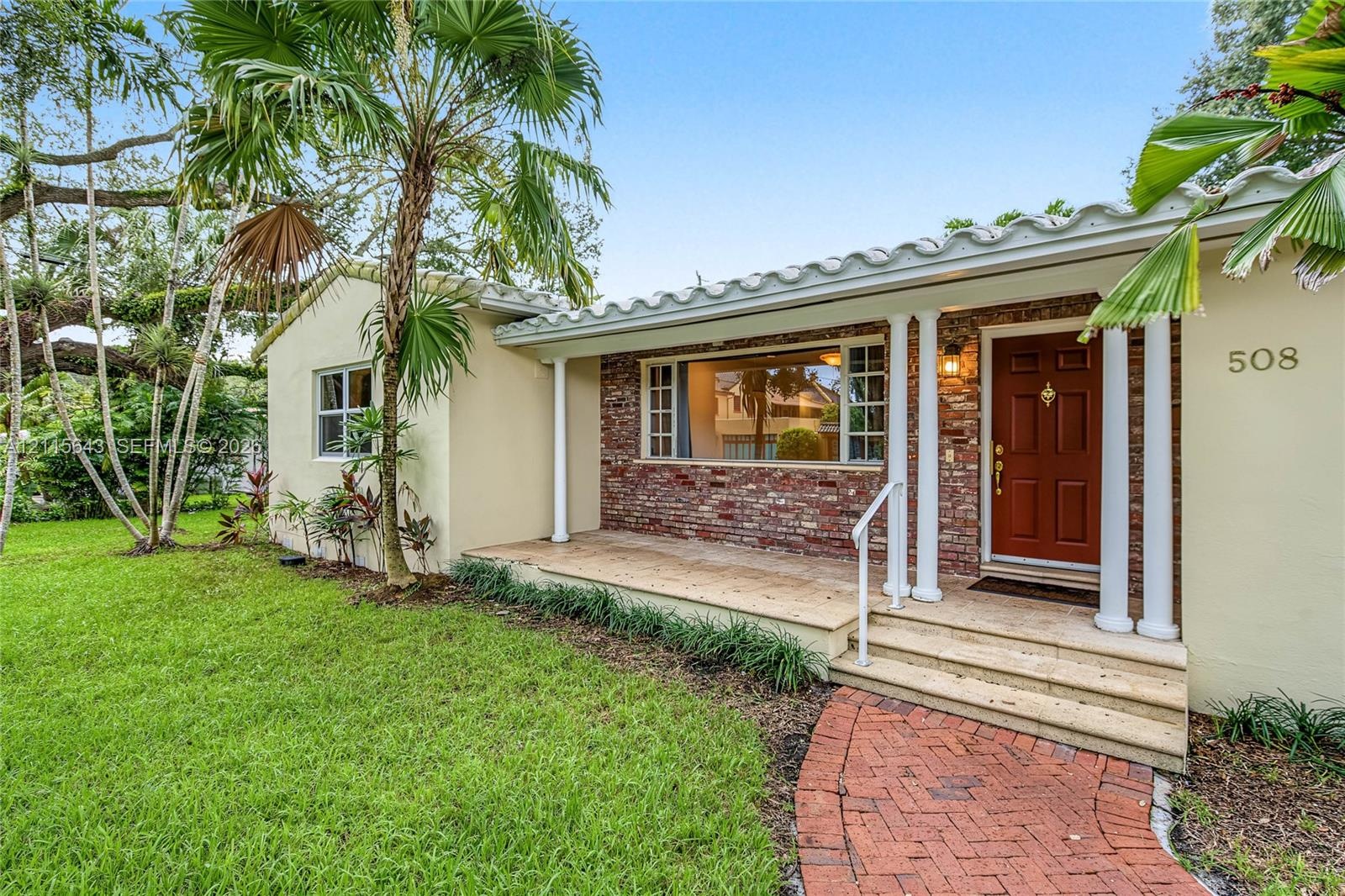 Stucco exterior featuring a red brick facade, covered front porch with classic columns, barrel tile roofline, and a brick paver walkway