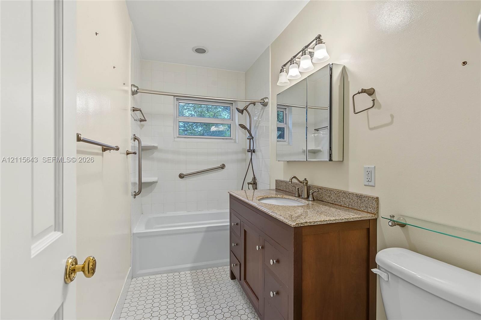 Bathroom featuring a vanity with wood-finish cabinetry, stone-composite countertop, integrated medicine cabinet, tile-surround bathtub, and geometric 