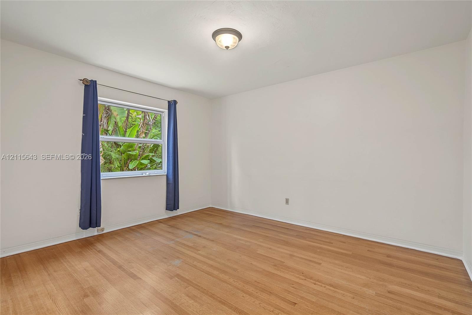 Wood-finish flooring, neutral wall tones, and single-pane window with natural exterior foliage