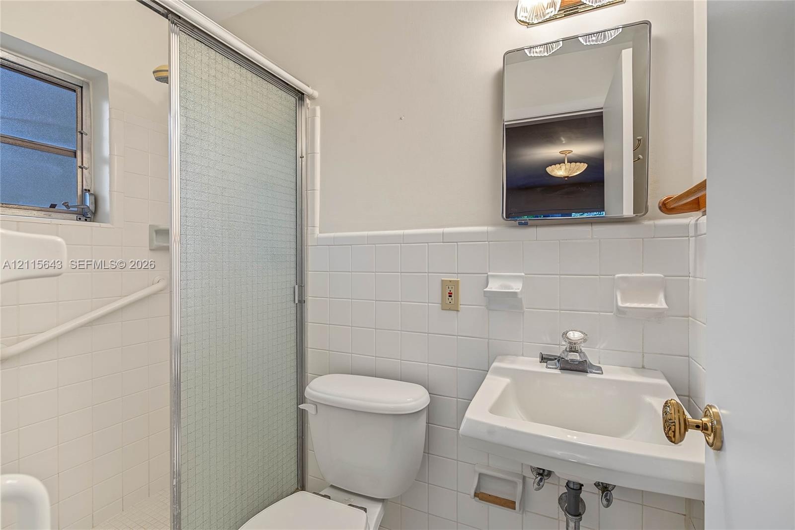 Bathroom featuring white square tile wall cladding, a wall-mounted sink with chrome faucet, a recessed medicine cabinet, and a shower enclosure with a