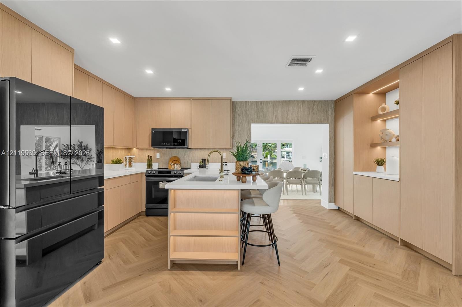 Kitchen featuring light wood-finish cabinetry, herringbone-patterned wood flooring, a central island with an integrated sink and under-counter lightin