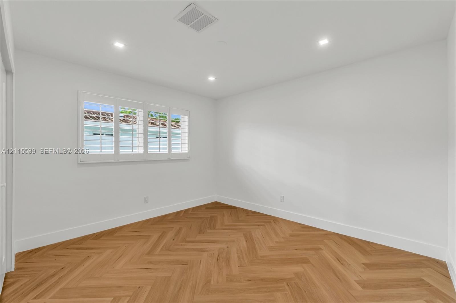 Interior room featuring wood-finish flooring in a herringbone pattern, recessed lighting, and multi-panel plantation shutters