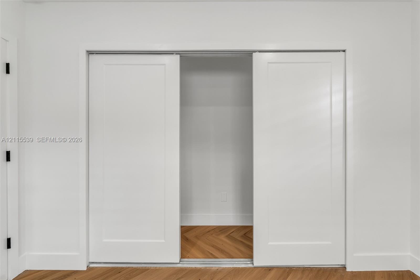 Dual sliding Shaker-style doors with a matte white finish and herringbone wood-finish flooring