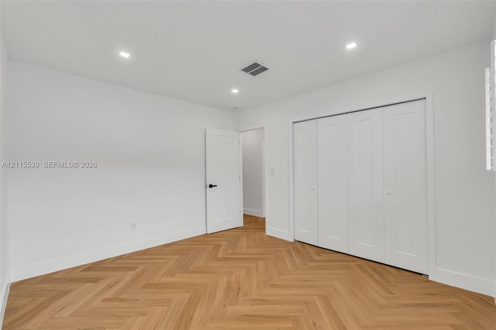 Neutral interior featuring herringbone wood-finish flooring, recessed lighting, and a multi-panel closet with crisp white doors