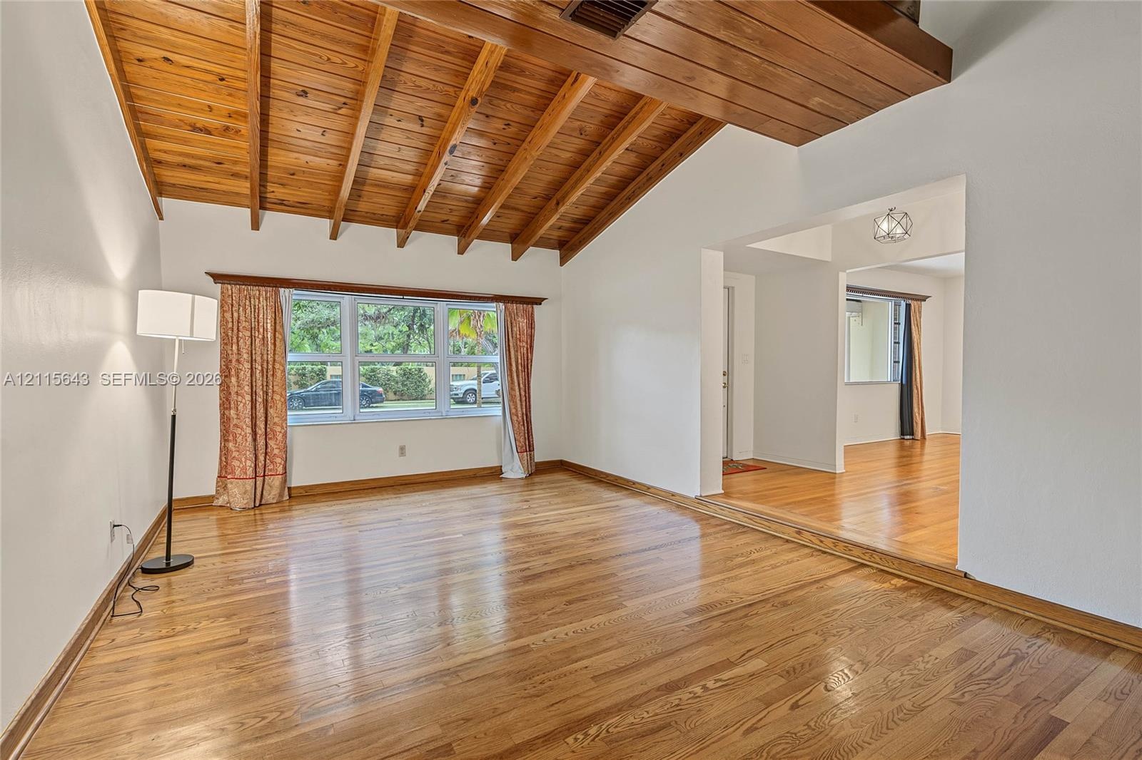 Vaulted ceiling featuring exposed wood beams, plank wood-finish flooring, and expansive window configuration