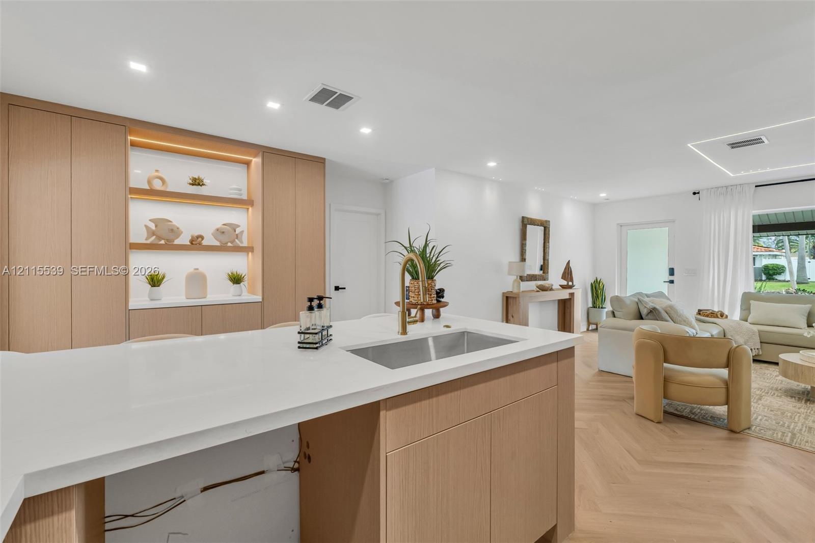 Kitchen featuring light wood-finish cabinetry, a white quartz countertop, an undermount stainless steel sink with a brass faucet, built-in recessed sh