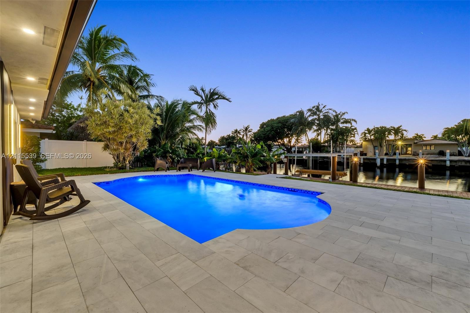 In-ground swimming pool featuring a large stone-paver deck, waterfront bulkhead, and tropical landscaping