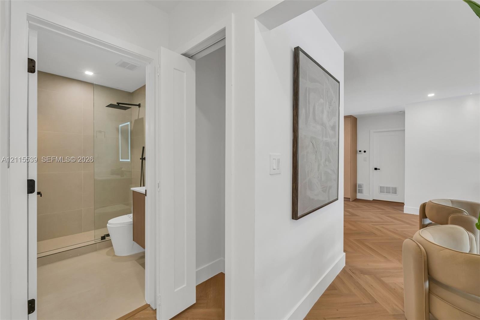 Herringbone wood-finish flooring, walk-in shower with large-format tile, frameless glass shower enclosure, matte black rainfall showerhead, and integr