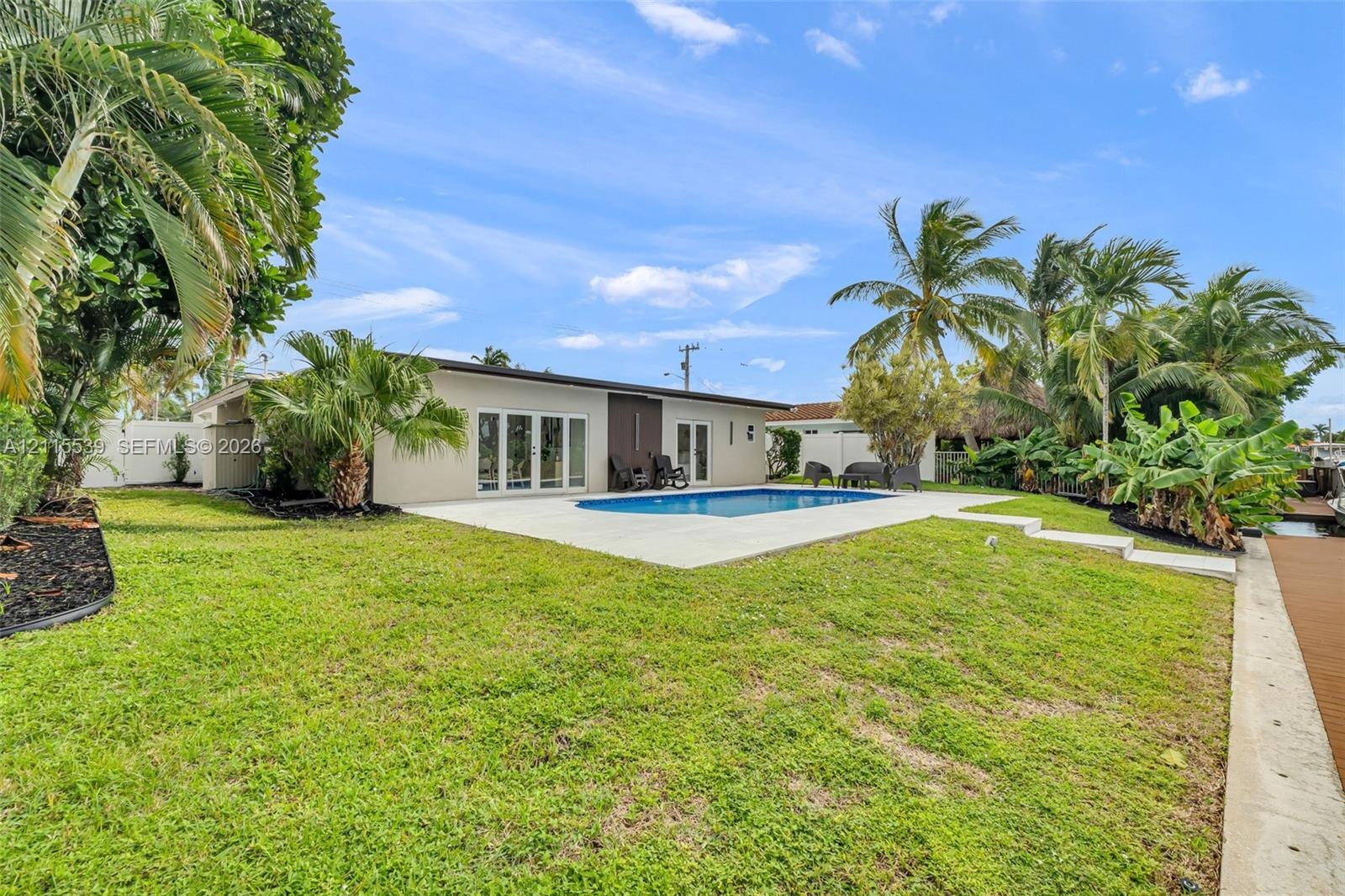 Backyard featuring a concrete pool deck, in-ground swimming pool, manicured lawn, tropical landscaping, and a waterfront bulkhead