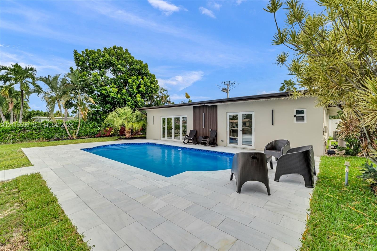 In-ground swimming pool with light-toned stone paver decking, exterior wall lighting, and double-glass door entry