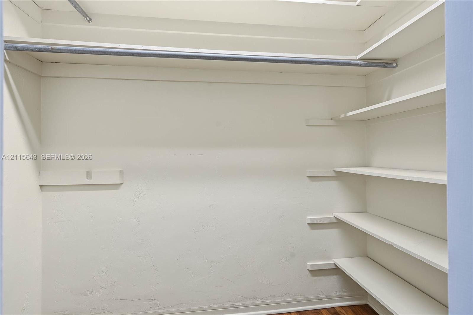 Storage closet featuring a full-width metal clothing rod, upper shelving, and a tiered side shelving system with white-painted finishes